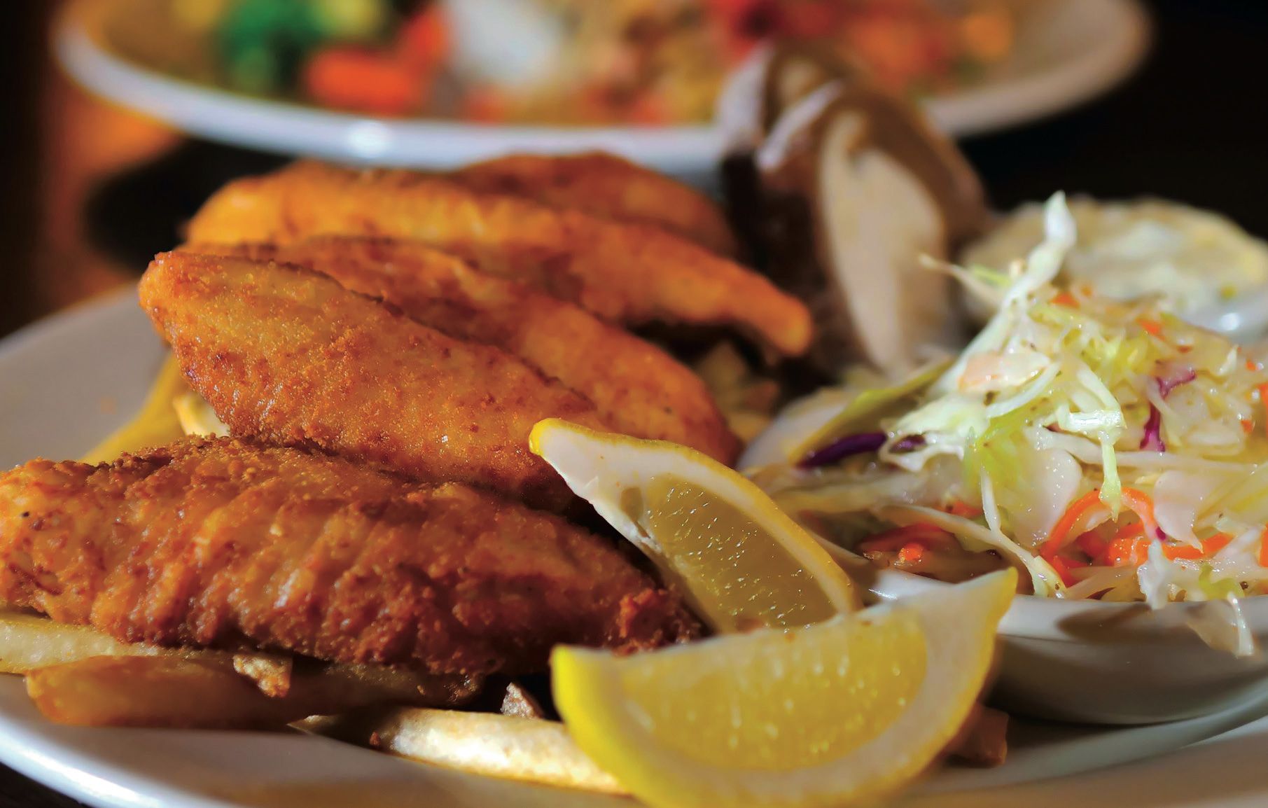 A crispy battered white fish with lemon wedges on a plate with coleslaw.