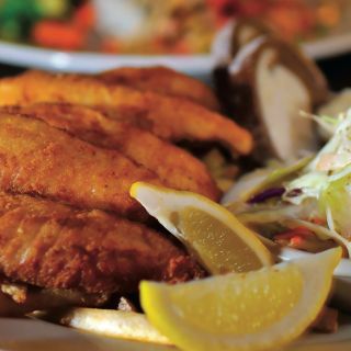 A crispy battered white fish with lemon wedges on a plate with coleslaw.